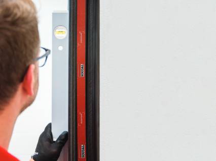 Installer checking a window frame with a spirit level, with red Soudal tape applied next to the wall